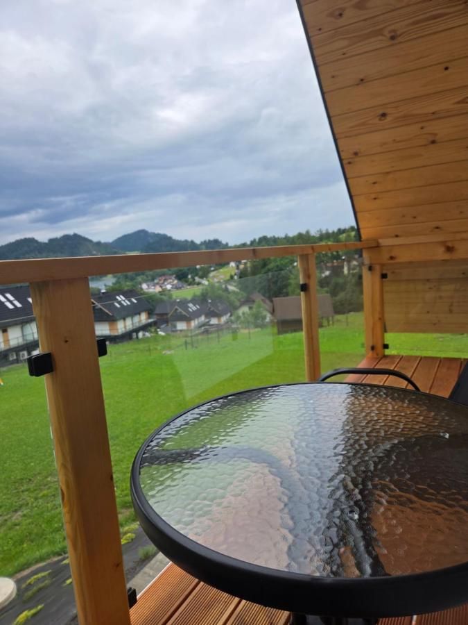 Szklany stolik na balkonie z drewnianą balustradą, w tle łąka i góry