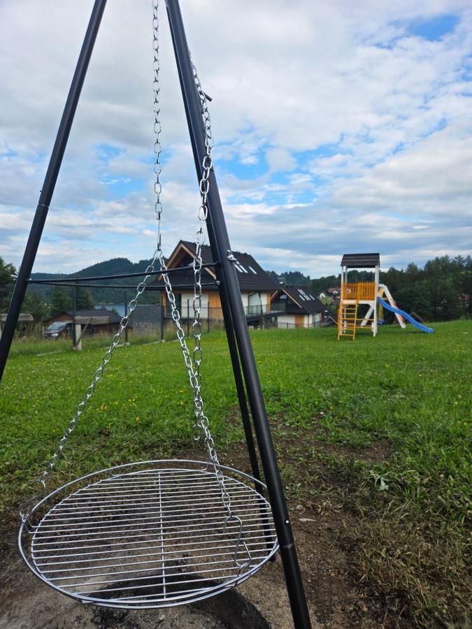 Grill na trójnogu na łące, w tle domy i góry